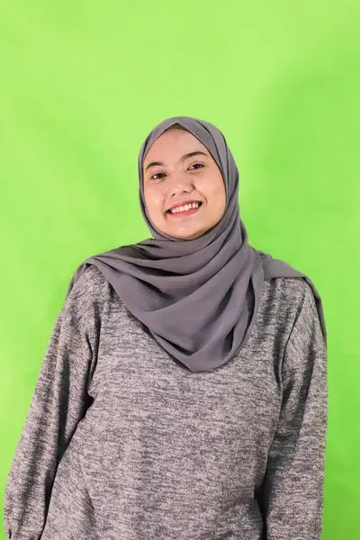 Müslüman kadın başını yeşil arka plana yaslarken içten bir şekilde gülümsüyor.