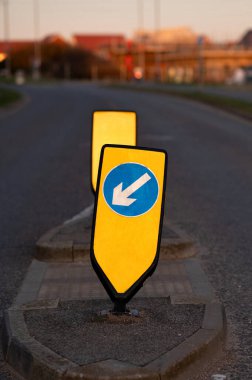 İngiltere 'de bir banliyö caddesinde sarı bir arka planda beyaz ve mavi oklu sol bollard tutun. 