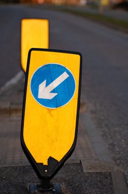 İngiltere 'de bir banliyö caddesinde sarı bir arka planda beyaz ve mavi oklu sol bollard tutun. 