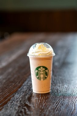 A Starbucks frappuccino-style beverage topped with whipped cream, placed on a rustic wooden surface with no people in frame.