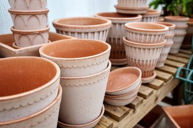 Çeşit çeşit kil ve seramik saksılar farklı şekillerde ve desenler açık havada ahşap raflarda dizilmiş..