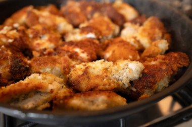 Yakından bakınca altın sarısı kahverengi tavuğun gaz ocağında siyah bir tavada kızardığını görüyoruz. Çıtır çıtır kaplama ve cızırdayan yağ tabağın hazır olduğunu gösteriyor. Yüksek kalite fotoğraf