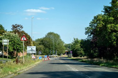 Corby, Birleşik Krallık - 10 Ağustos 2025: Güneşli bir günde açık mavi gökyüzü altında trafik konileri ve yön işaretleriyle dolu bir yol.