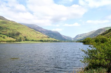 Önünde göl olan bir dağ vadisi manzarası, yeşil yamaçlar ve bulutlu yaz gökyüzü. Yüksek kalite fotoğraf