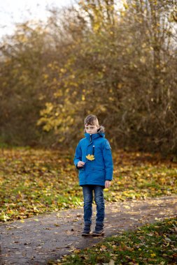 Sonbahar parkında sarı yaprak tutan çocuk..