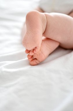 Yumuşak beyaz çarşaflarda dinlenen küçük bebek ayaklarının yakın çekimi.