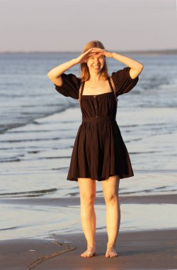 Genç bayan sahilde akşamdan zevk alır. Kız deniz kıyısında gün batımına hayran. Kavram: huzurlu bir akşam, güzel bir manzara. Yüksek kalite fotoğraf