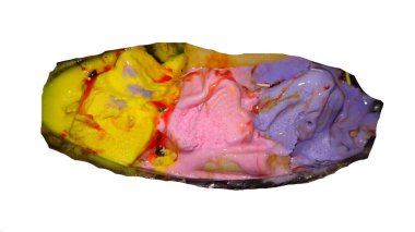 Üç kepçe dondurmanın canlı bir görüntüsü muz parçacıklı bir tabakta. Dondurma aromaları sarı, pembe ve mor renkli şerbetle kaplı..