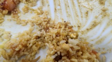 Beyaz bir tabakta sebzeli ve soslu arta kalan pirinç tanelerini ve yemek artıklarını gösteren yakın plan..