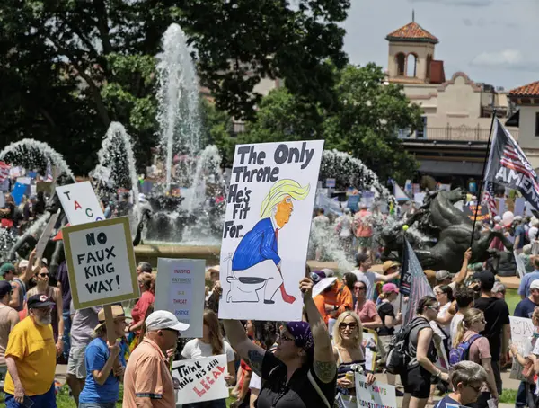 Tuvalette siyasi bir figürün tasviri de dahil olmak üzere çeşitli katılımcıların tabela taşıdığı büyük bir protesto. Sahne, fıskiyeli ve ağaçlı bir park..