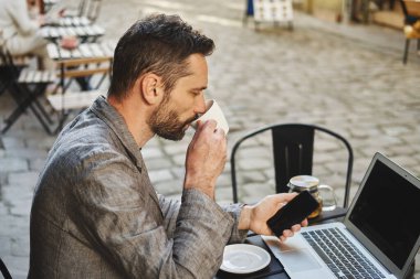 Beyaz bir erkek sokak kafeteryasında bir bilgisayarda çalışıyor. Uzak çalışma konsepti.