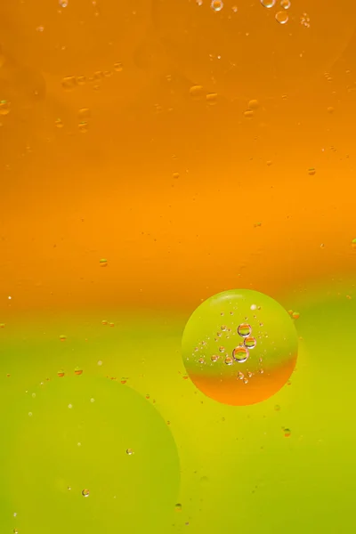 Macro drops of oil on the surface of the water. bright orange-green background for advertising products. copy space and gradient. Vertical photo