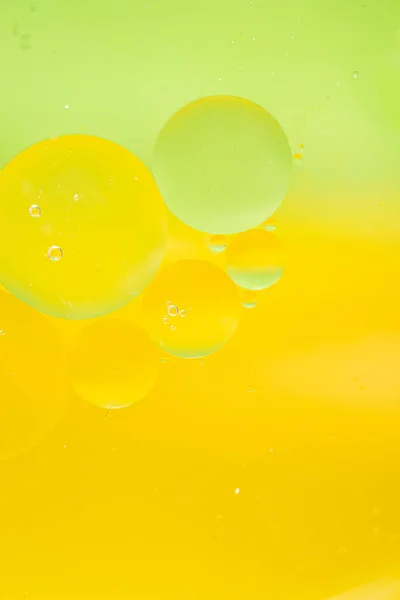 Macro drops of oil on the surface of the water. bright yellow-green background for advertising products. copy space and gradient. Vertical photo