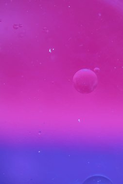Bright gradient background - magenta color turning into blue. Macro drops of oil on the surface of the water. Vertical cosmetic background for promotional products. copy space 