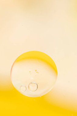 Abstract background in pale yellow colors. Macro drops of oil on the surface of the water. Delicate cosmetic background for promotional products. copy space and gradient. Vertical photo