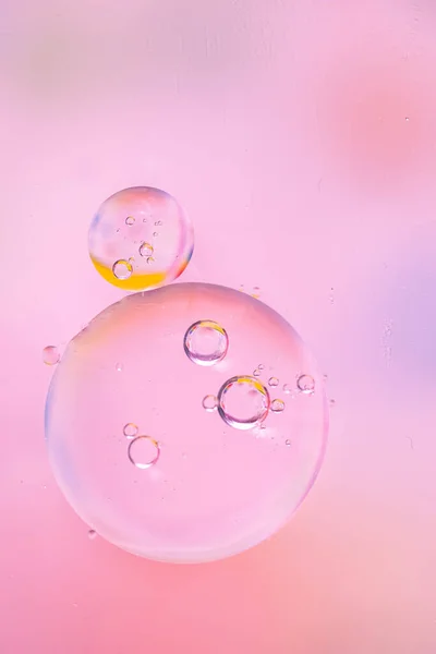 Macro drops of oil on the surface of the water. Delicate cosmetic background for promotional products in pale pink colors. copy space and gradient. Vertical photo