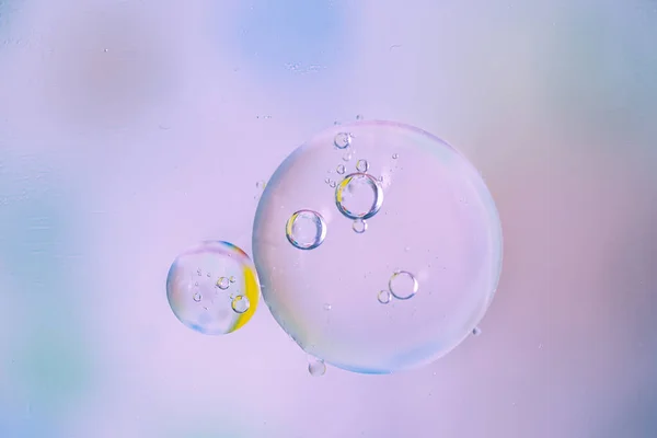 Macro drops of oil on the surface of the water. Delicate cosmetic background for promotional products in pale blue-violet colors. copy space and gradient.