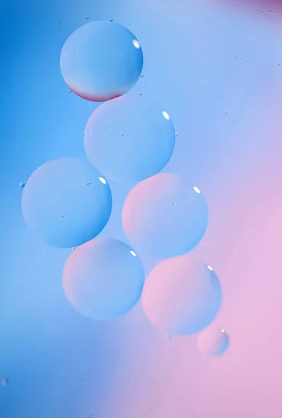 Macro drops of oil on the surface of the water. Delicate cosmetic bubbles background for advertising cosmetic products in soft blue pink tones, copy space and gradient. Vertical photo