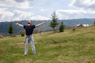 Dağların arka planında açık bir alanda mutlu bir beyaz adam. O, kollarını açtı ve gözlerini kapattı. Doğa ve akıl sağlığı ile birlik kavramı 