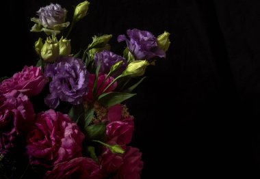 Durgun hayat. Siyah arka planda bir buket çiçek gülleri ve lisianthus. Loy anahtar fotoğrafı. Estetik fotoğraf. Bulanık arkaplan 