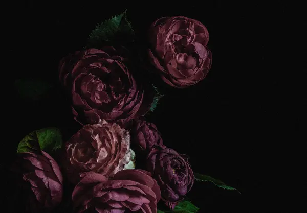 Moody flowers. Vintage bouquet of dark roses on a black background. Blur and selective focus. Low key photo