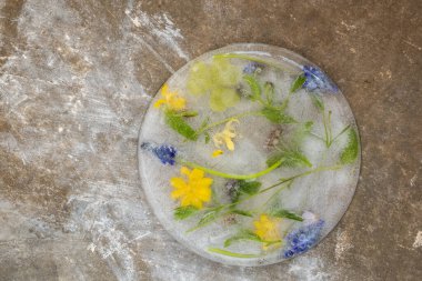 Renkli çiçekler ve yeşilliklerle kaplı yuvarlak, berrak buz bloğu desenli, kırsal bir yüzeye yerleştirilmiş.. 