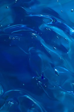 Kozmetik ürünlerin jel dokusunu kapat. Koyu mavi arka planda köpüklü şeffaf krem. makro fotoğraf. bulanık ve seçici odak. 