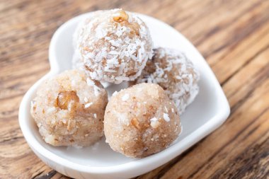 Kırsal bir masada beyaz kalp şeklinde bir tabakta servis edilen beş hindistan cevizi saadet topunun üst görüntüsü. Sağlıklı atıştırmalık ya da tatlı teması için mükemmel..