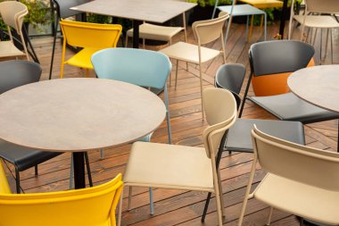 Bir sürü renkli boş sandalye ve ahşap bir verandaya dizilmiş yuvarlak masalar. Modern oturma alanı ziyaretçiler için hazır, kafeler ve açık hava etkinlikleri için mükemmel..