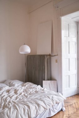 Beyaz bir yatak odası, modern bir lamba ve yumuşak doğal bir ışık. Minimalizm ve konforlu basit bir dekor..