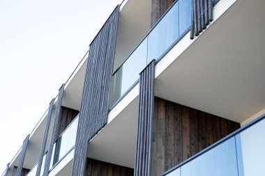 Ahşap paneller ve cam balkonların yer aldığı çağdaş bir konut binasının alçak açılı görüntüsü, minimalist mimari tasarımı sergiliyor..