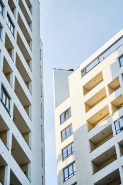 Minimalist, beyaz, balkonlu apartmanların alçak açılı görüntüsü, açık mavi gökyüzüne karşı kurulmuş. Modern şehir mimarisi ve geometrik çizgilerin gösterimi.