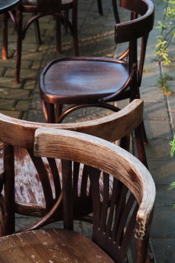 Dışarıdaki bir kafenin terasına bir çift köhne, yıpranmış tahta sandalye. Etrafı yemyeşil saksılarla çevrili olan manzara sıcaklık ve rahatlama yayar.. 