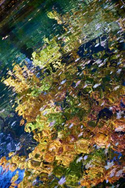 Abstract view of autumn trees reflected in rippling water, blending vibrant green, orange, and blue hues to create a mesmerizing, wavy pattern. clipart