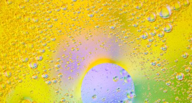 Suyun içinde parlak sarı, yeşil ve mor tonlara sahip renkli yağ kabarcıkları içeren parlak soyut bir arka plan. Yaratıcı tasarım projeleri ve modern görseller için ideal. Renkli balon duvar kağıdı 