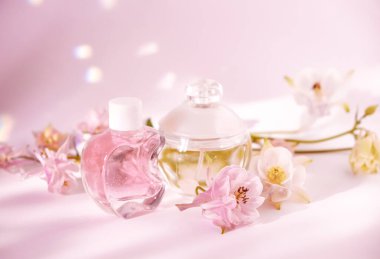 Two elegant cosmetic bottles, one pink and one clear, surrounded by soft pink and white flowers on a pastel pink background. Ideal for beauty, skincare, or wellness themes showcasing femininity  clipart