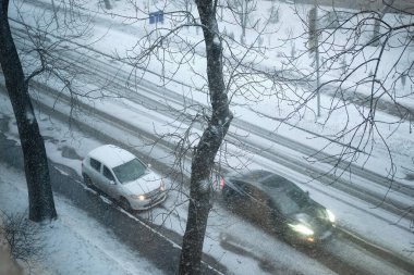 Kış kar yağışı sırasında iki araba karla kaplı bir yol boyunca seyahat eder. Çıplak ağaç dalları sahneyi çerçeveleyerek kasvetli ve kentsel bir kış ortamı yaratıyor. Bulanık hareket 