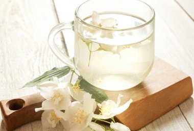 A steaming glass cup of jasmine tea adorned with fresh jasmine flowers, placed on a rustic wooden board. Perfect for wellness, natural beauty, and food photography themes.  clipart