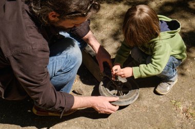 Baba ve küçük oğlu arka bahçede bisiklet tekerleğini tamir ederken birlikte çalışıyorlar. Takım çalışmasına odaklanma ve dışarıda pratik beceriler öğrenme anı. Takım çalışmasını dışarıda onarın.