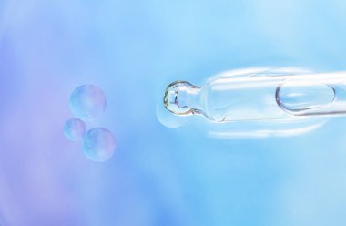 Sonunda cam pipet ve şeffaf sıvı damlası ve açık maviden açık mora doğru mavi bir arkaplanda üç kabarcık. Yumuşak ışık, camda parıltı, minimalist stil. en üstteki görünüm