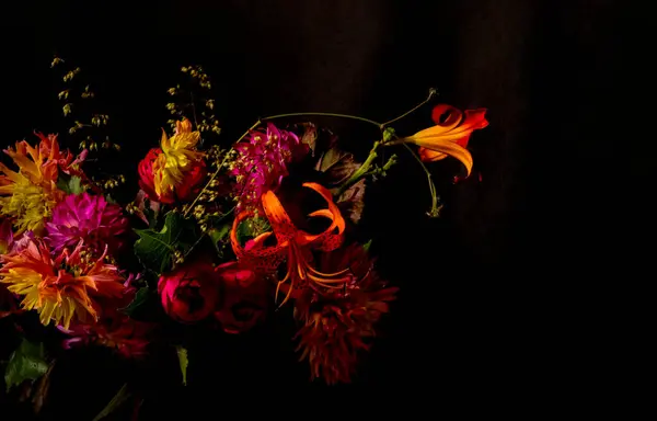 Karanlık bir arka planda parlak bir buket çiçeğin yakın çekimi. Buket sarı, pembe, turuncu ve kırmızı da dahil olmak üzere farklı tonlarda çiçeklerden oluşur. Kapsama alanı