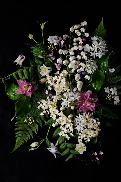 Zarif bir siyah arkaplan karşısında çeşitli canlı çiçekler ve yemyeşil yapraklardan oluşan güzel bir buket, çarpıcı bir kontrastlık yaratır.