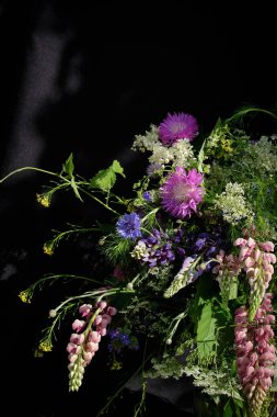 Dramatik çiçek buketi, yabani devedikenleri, çiçek yaprakları, tilki eldivenleri ve siyah arka planda yeşillik. Doğal ve karamsar bahçe tarzı. 