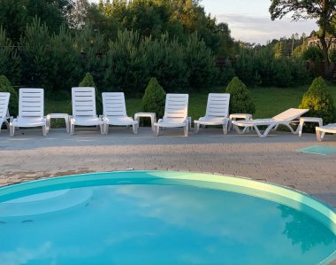 Beyaz plastik güneş pansiyonları açık mavi yüzme havuzunun yanındaki açık hava oteli avlusunda. Yaz tatili kavramı. 