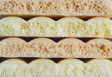 Makro fotoğraf, yumuşak, gözenekli ve kahverengi renkli havadar çikolatalı kek katmanlarını gösteriyor. Ayrıntılı kırıntı ve kabarık yapıyı vurgulayan doğal ışık ile yan görünüm