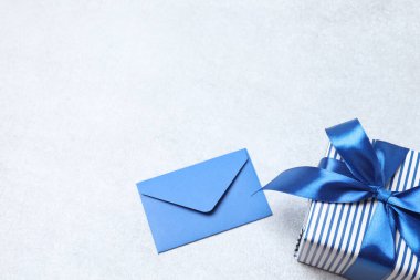Mavi bir zarf, beyaz bir hediye kutusu ve mavi bir masa üzerinde bir fiyonk.