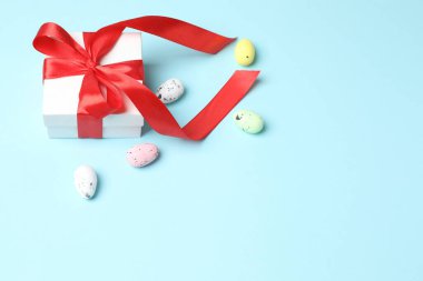 Mavi arka planda hediye kutusunda kurdeleli beyaz Paskalya yumurtaları.