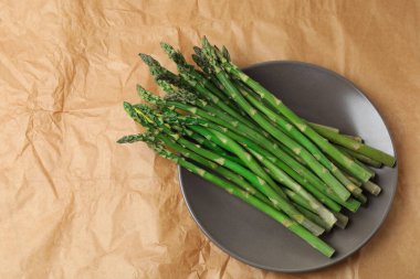 Kahverengi bir kasede beyaz tabakta yeşil kuşkonmaz. en üstteki görünüm.