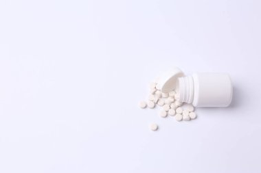 Beyaz arka planda beyaz bir şişede beyaz haplar.