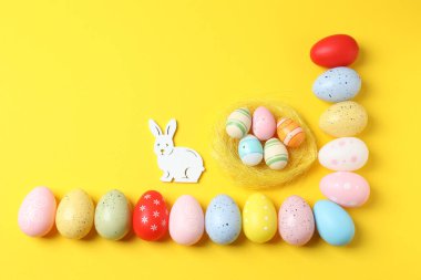 Renkli boyalı yumurtalar ve sarı arka planda farklı paskalya süslemeleri olan paskalya yumurtaları. düz yatış, üst görünüm
